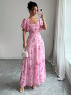 Woman taking a mirror selfie wearing a pink floral dress in a room with white curtains.